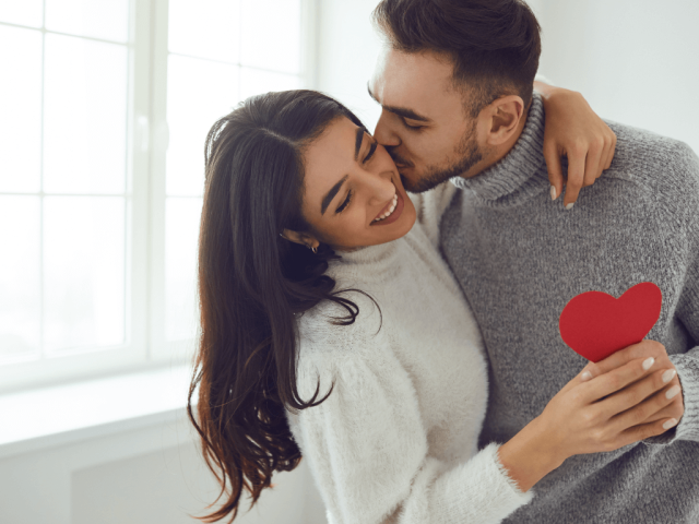 man lovingly kissing womans cheek and holding a cutout heart