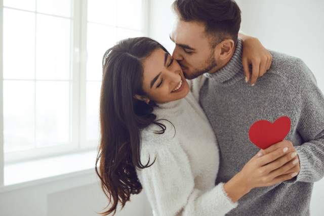 man lovingly kissing womans cheek and holding a cutout heart