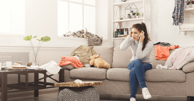 woman is on couch on the phone with a dirty, messy house.